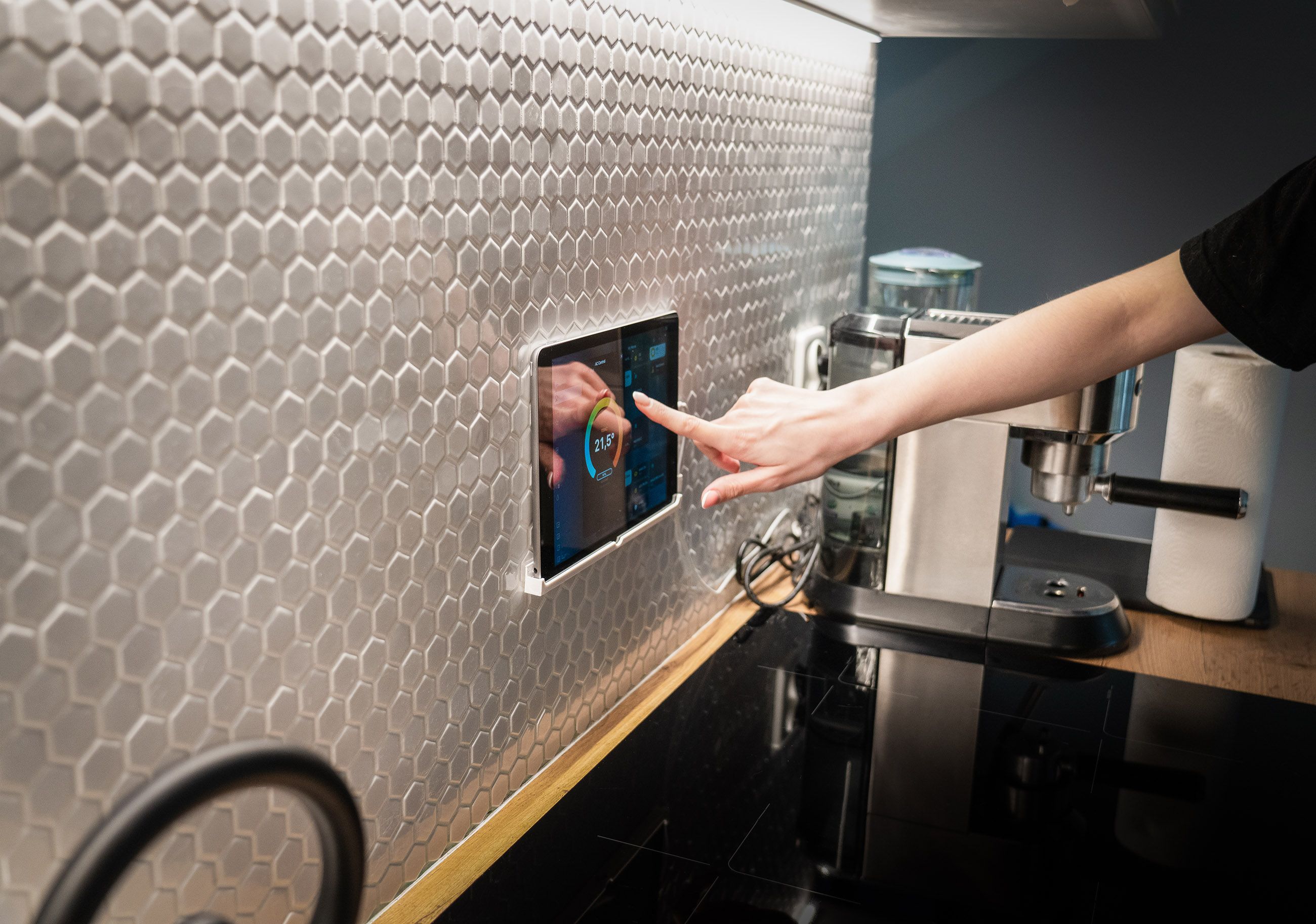 A modern kitchen with a touchscreen smart home control panel integrated into a hexagon-patterned wall